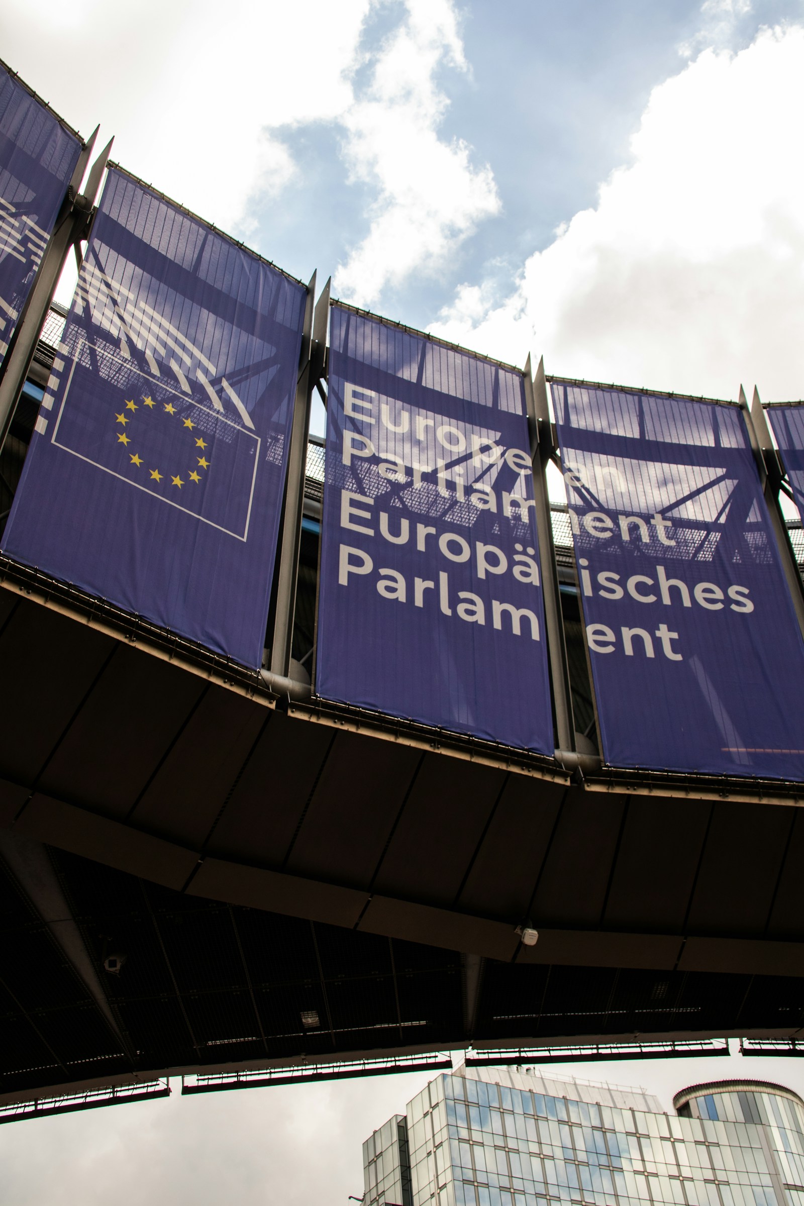 European Parliament building with EU flags under a cloudy sky